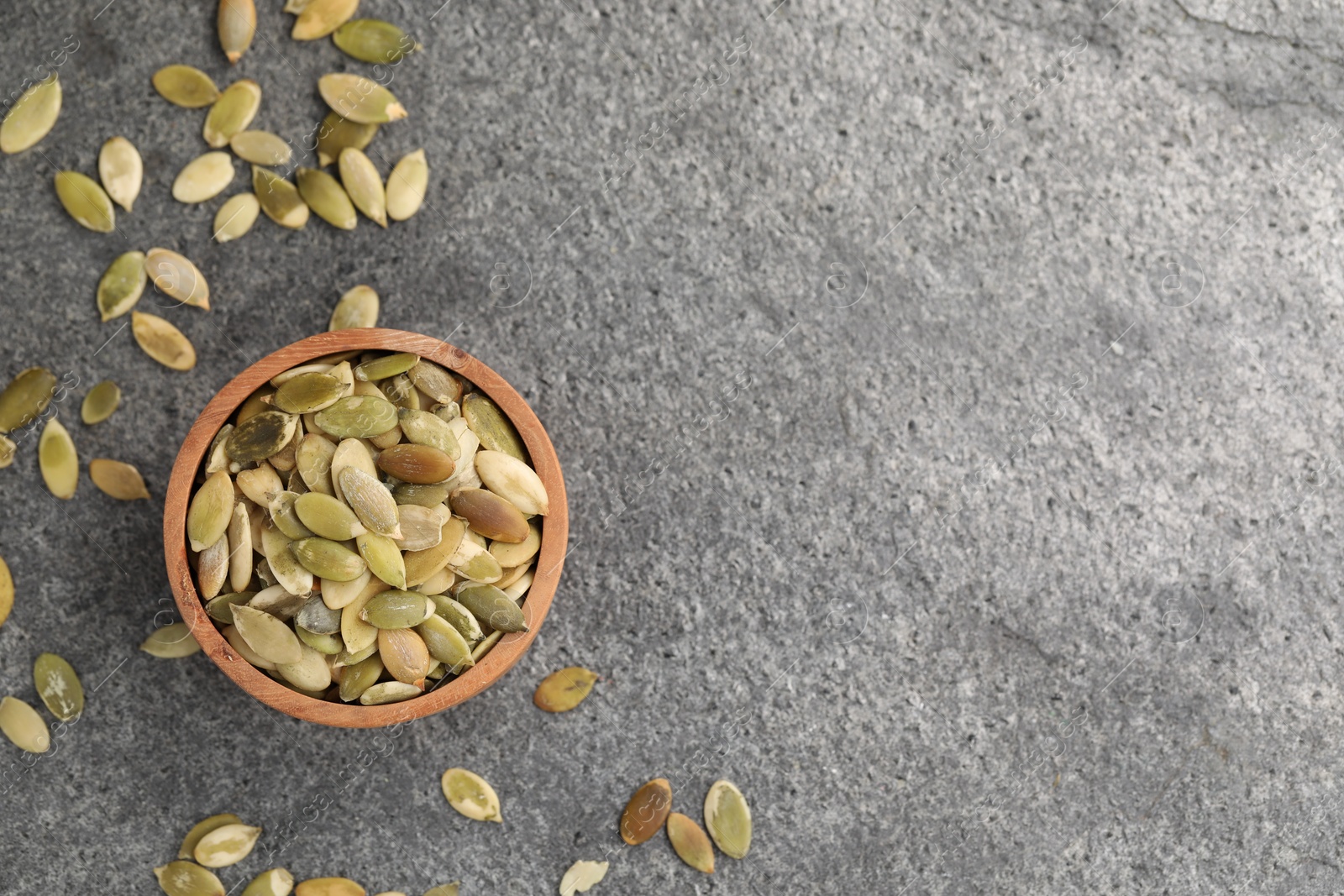 Photo of Wooden bowl with peeled pumpkin seeds on grey table, flat lay. Space for text