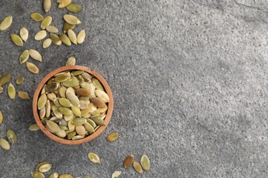 Photo of Wooden bowl with peeled pumpkin seeds on grey table, flat lay. Space for text