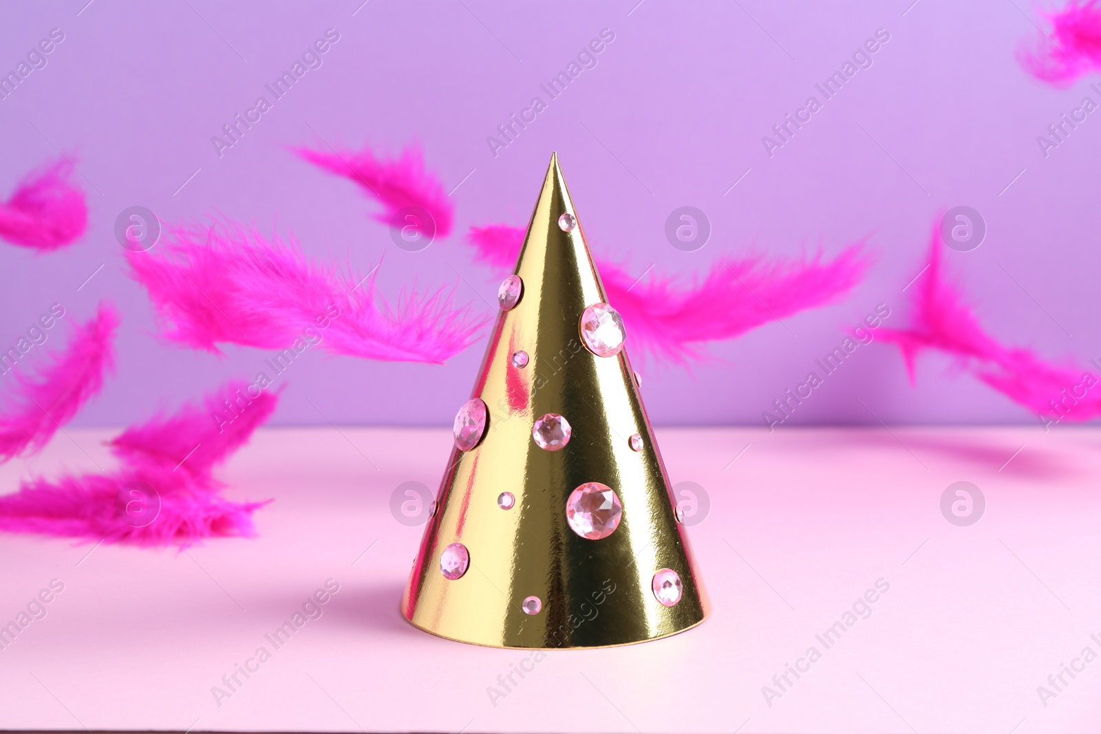 Photo of Golden party hat with rhinestones and bright feathers on color background