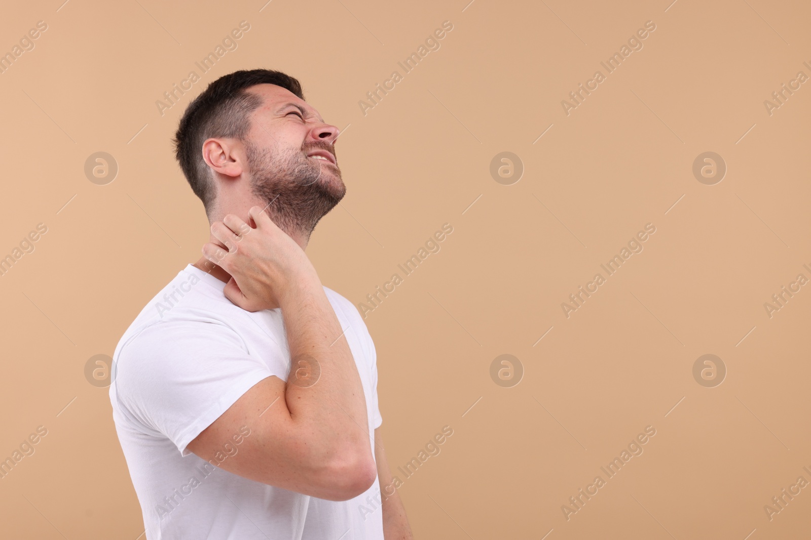 Photo of Allergy symptom. Man scratching his neck on light brown background. Space for text