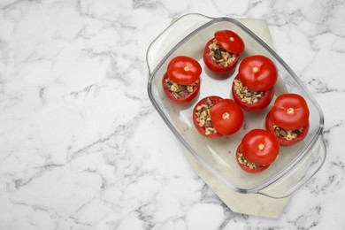 Photo of Delicious stuffed tomatoes with minced beef, bulgur and mushrooms in glass baking dish on white marble table, top view. Space for text
