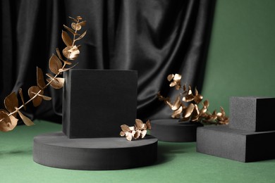 Photo of Black geometric figures and decorative golden leaves on green background. Stylish presentation for product