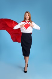 Photo of Confident businesswoman wearing superhero costume under suit on light blue background