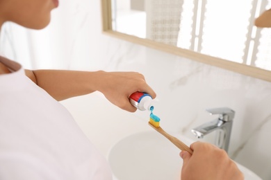 Photo of Woman applying toothpaste on brush in bathroom, closeup