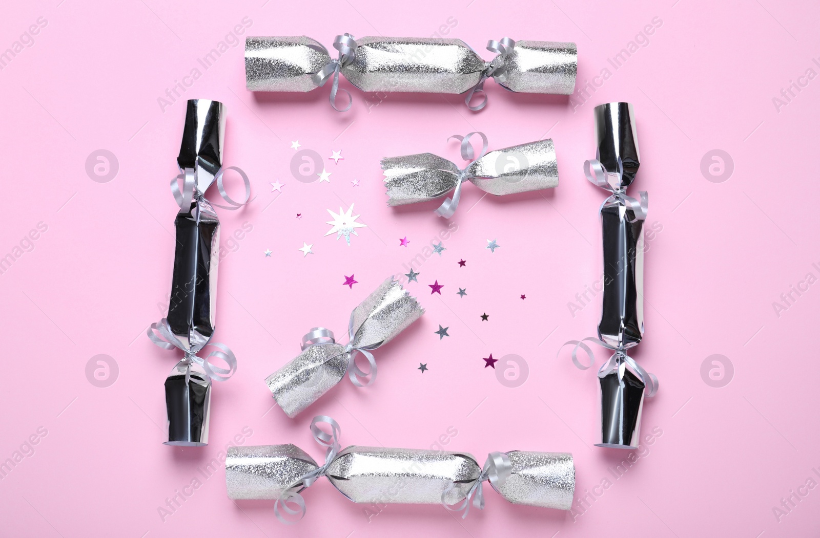 Photo of Silver Christmas crackers and shiny confetti on pink background, flat lay