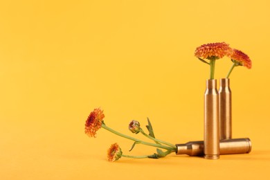 Bullet cartridge cases and beautiful chrysanthemum flowers on yellow background, space for text