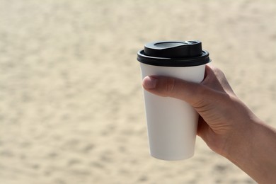 Photo of Woman with takeaway coffee cup on beach, closeup. Space for text