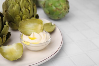 Photo of Delicious cooked artichokes with tasty sauce served on white tiled table, closeup. Space for text
