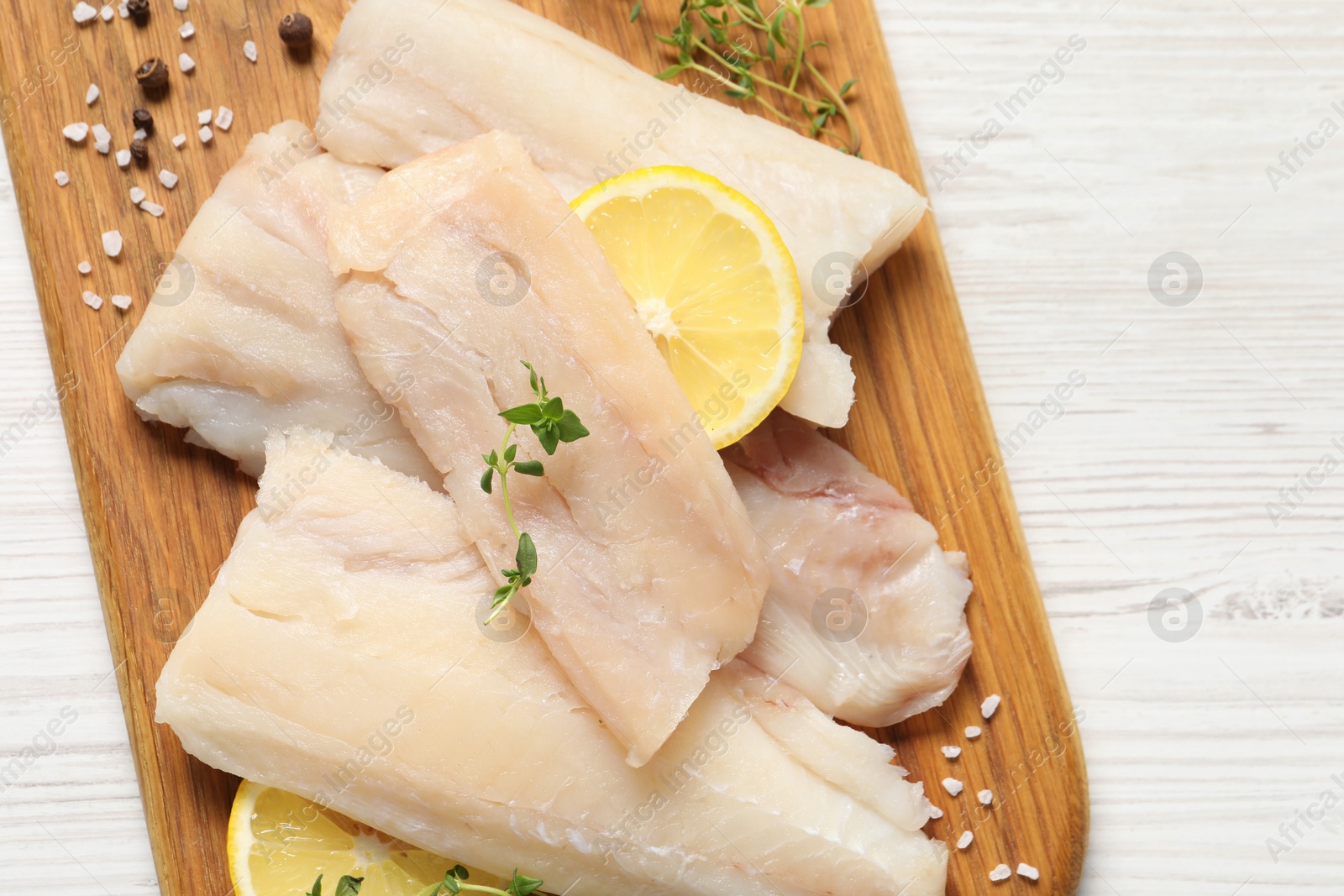 Photo of Pieces of raw cod fish, lemon and spices on white wooden table, top view