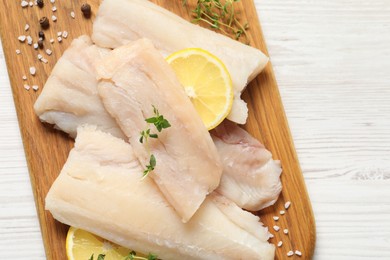 Photo of Pieces of raw cod fish, lemon and spices on white wooden table, top view