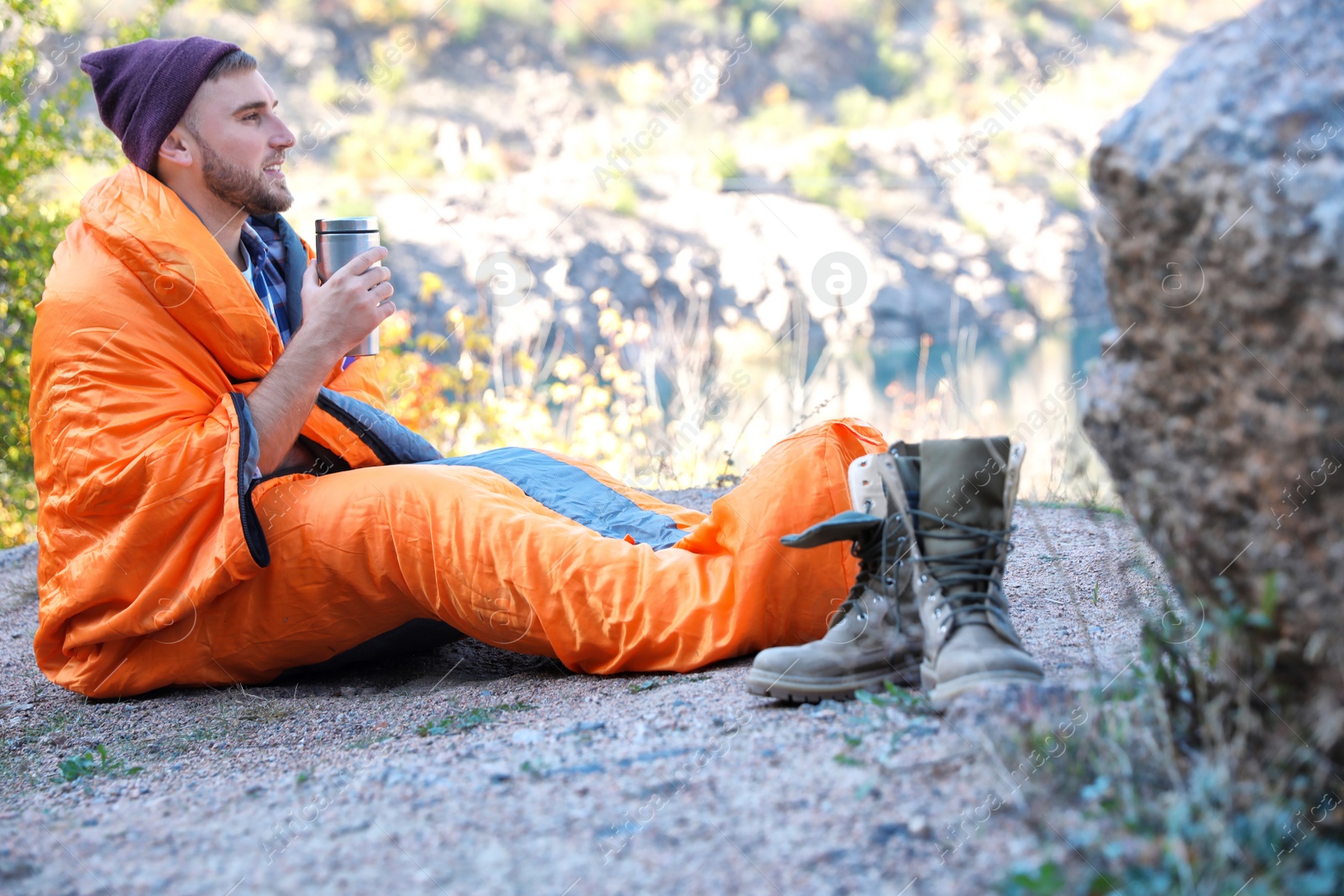 Photo of Male camper with thermos in sleeping bag outdoors