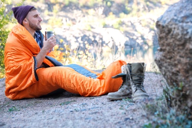 Photo of Male camper with thermos in sleeping bag outdoors