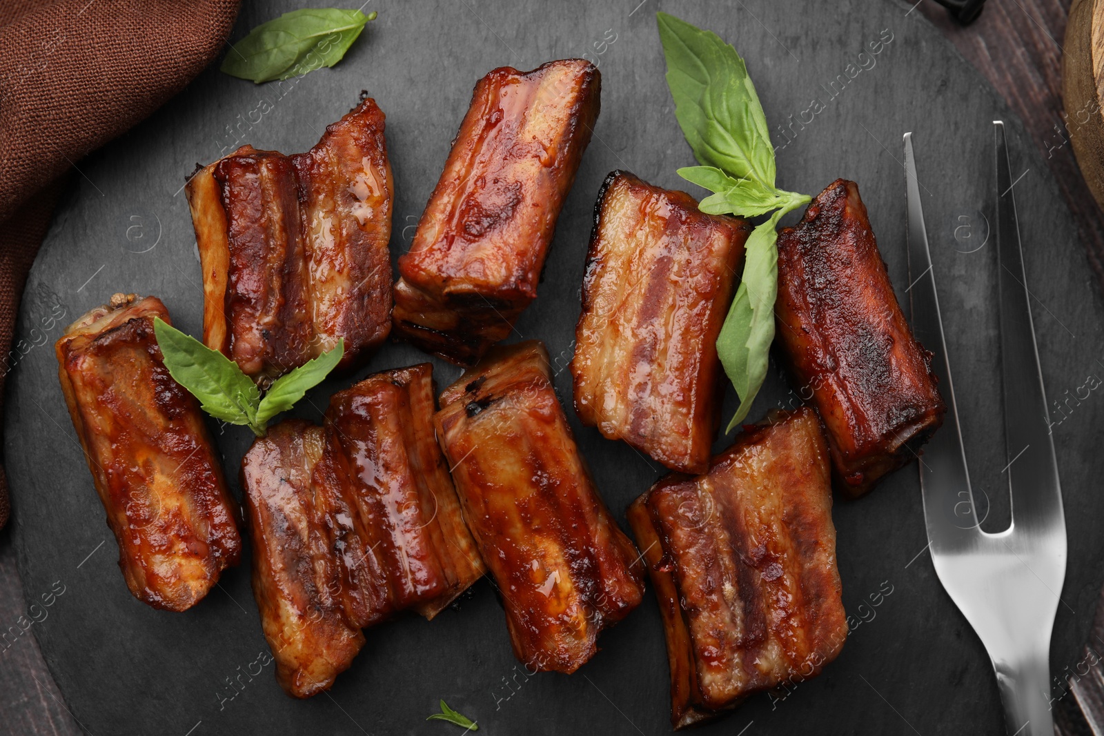 Photo of Tasty roasted pork ribs served on slate plate, flat lay
