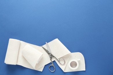 Photo of Medical bandage rolls, sticking plaster and scissors on blue background, flat lay. Space for text