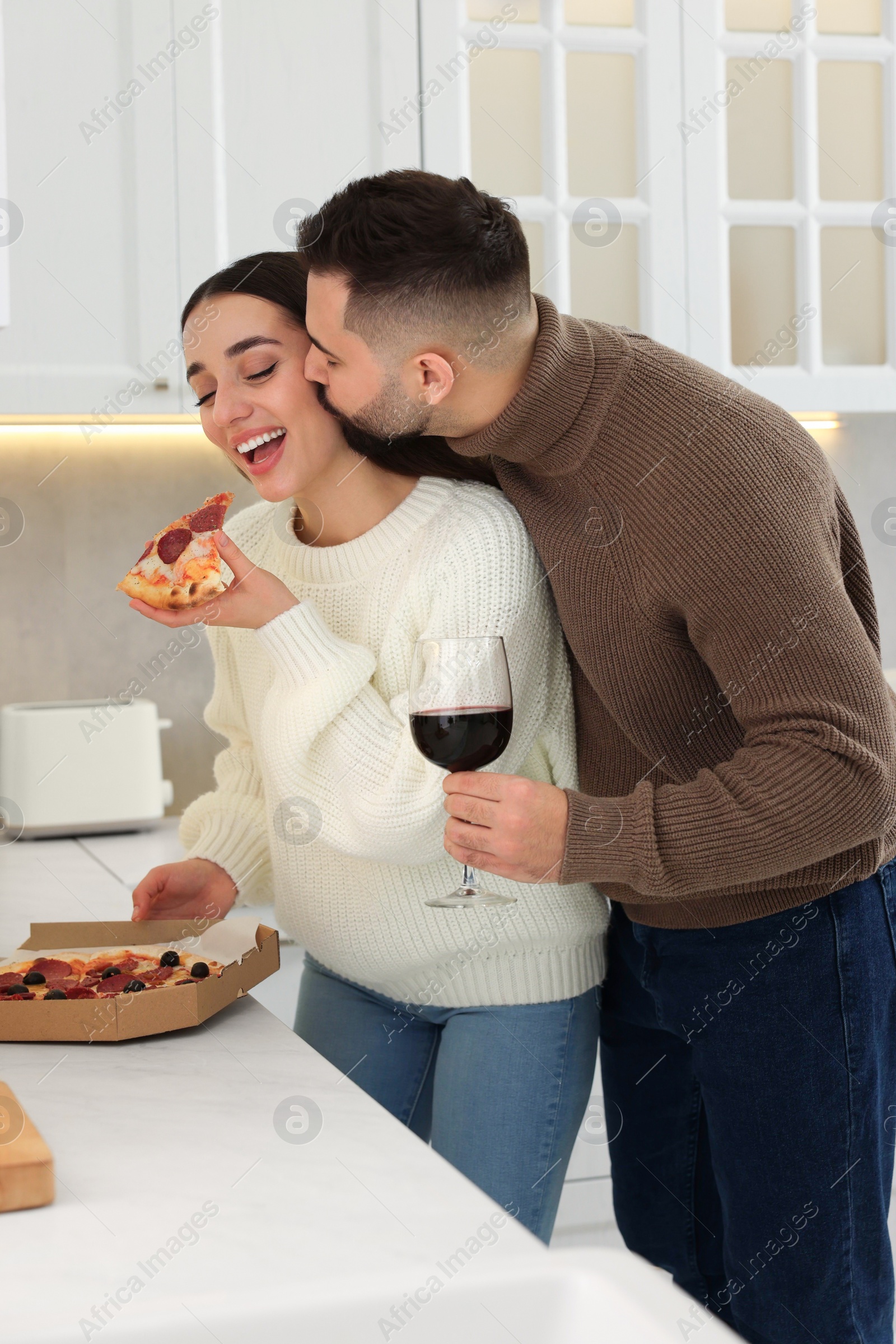 Photo of Happy young couple eating pizza and drinking wine in kitchen