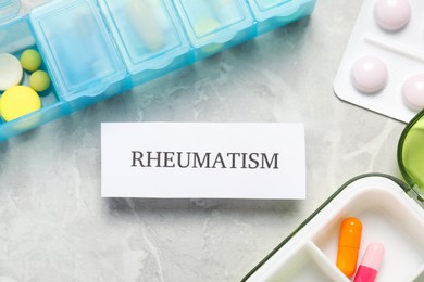 Card with word Rheumatism and pills on light gray marble table, flat lay