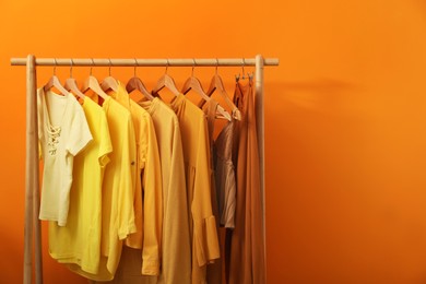 Photo of Rack with different stylish women's clothes near orange wall, space for text