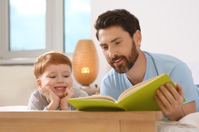 Photo of Father reading book with his child on bed at home