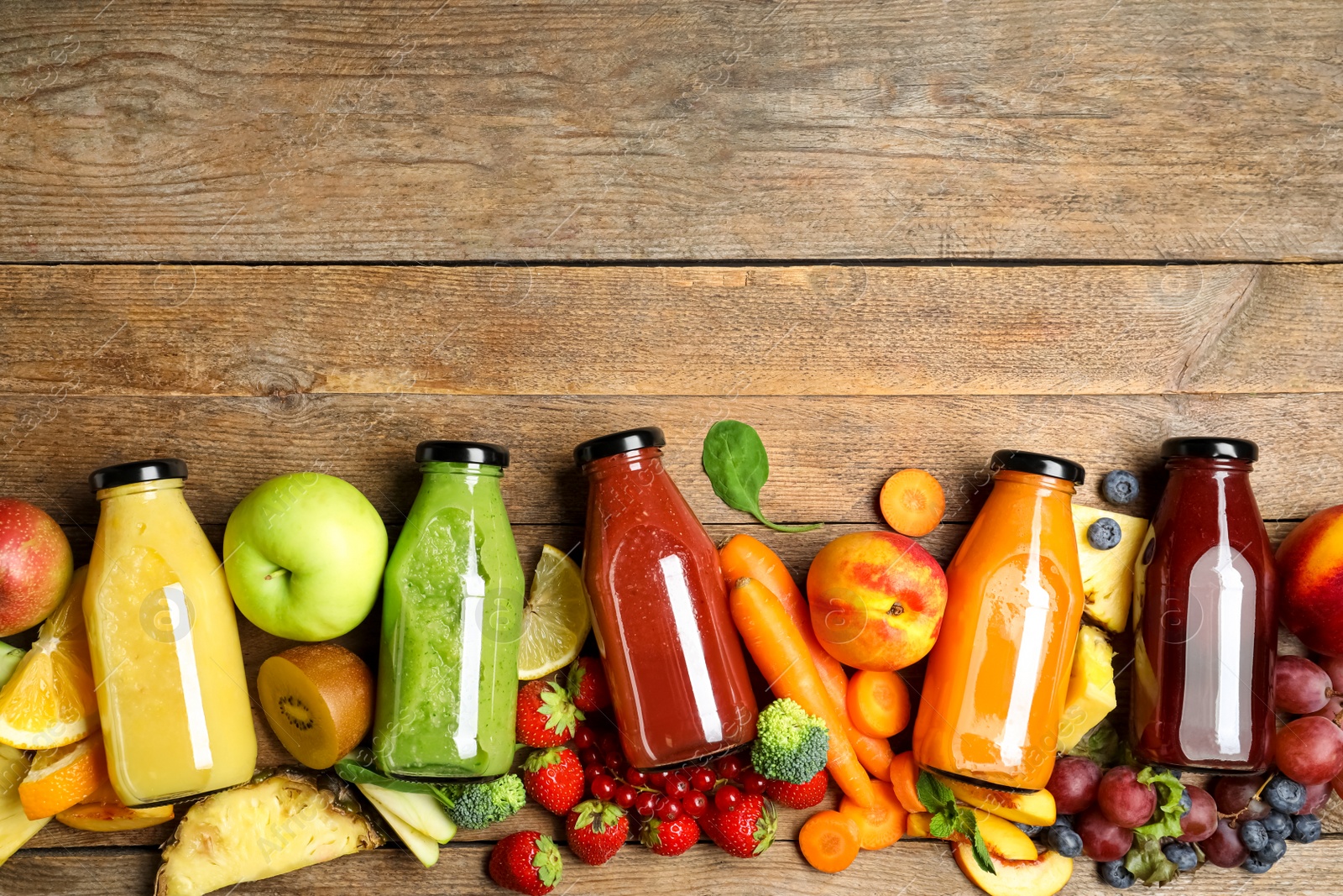 Photo of Bottles of delicious juices and fresh fruits on wooden table, flat lay. Space for text