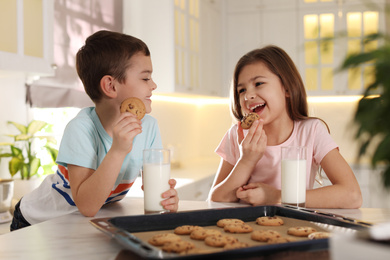 Photo of Cute little children eating cookies with milk in kitchen. Cooking pastry