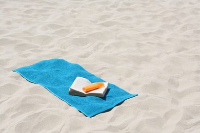 Blue towel, book and sunscreen on sandy beach. Space for text