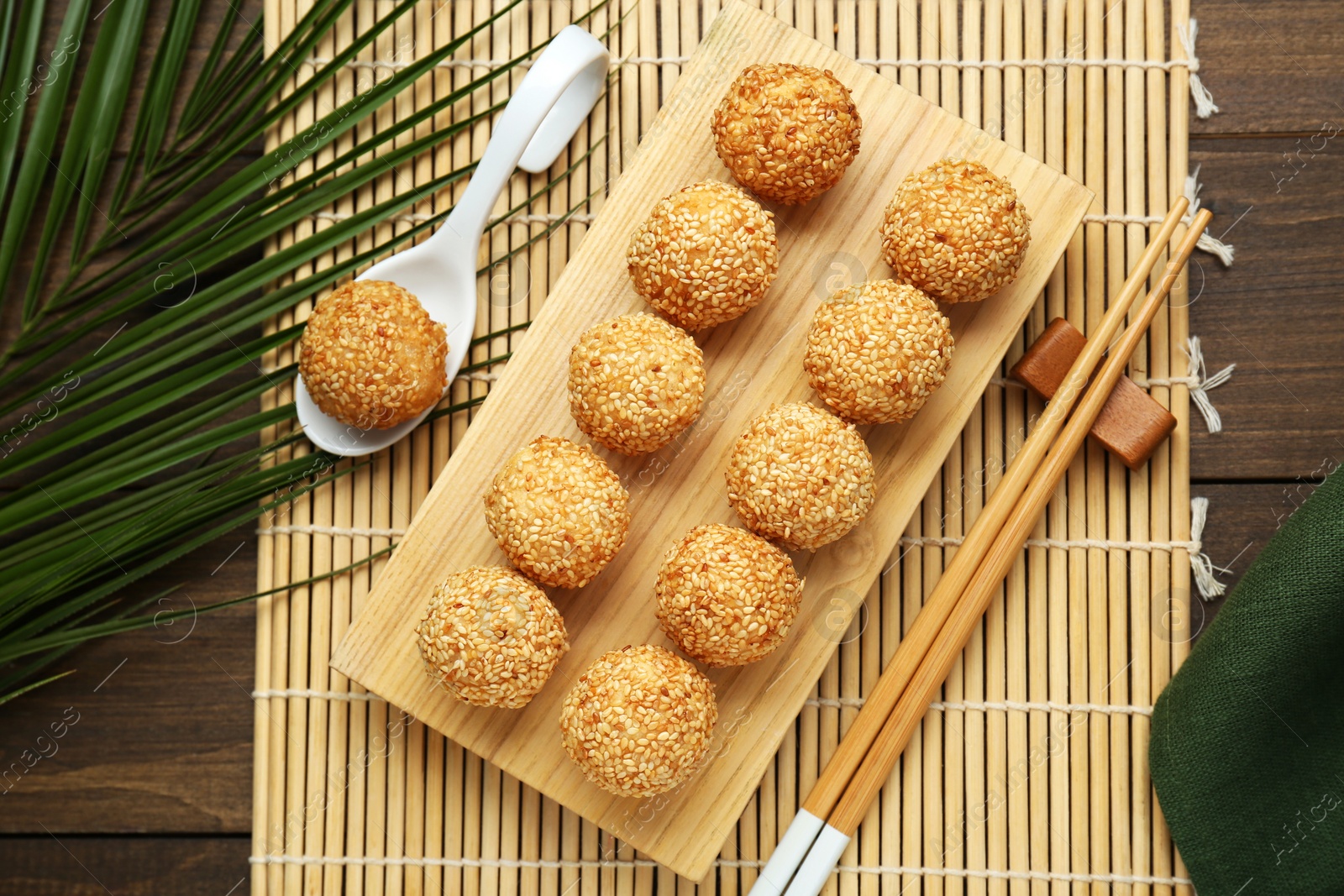 Photo of Delicious sesame balls, spoon, green leaves and chopsticks on wooden table, flat lay
