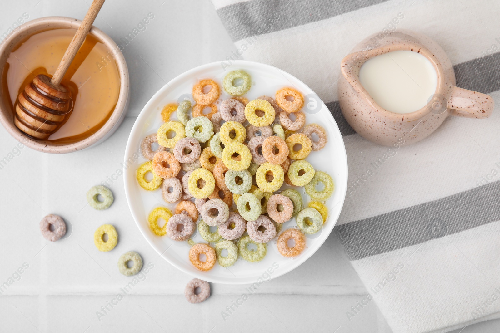 Photo of Cereal rings and milk in bowl on white tiled table, flat lay