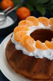 Photo of Homemade yogurt cake with tangerines and cream on blue wooden table, closeup