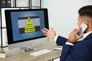 Photo of Office worker in front of computer with warning about virus attack on screen