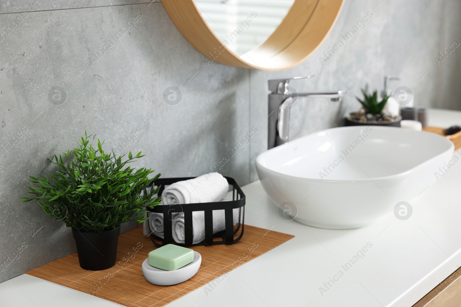 Photo of Potted artificial plant, rolled towels and soap near sink on bathroom vanity