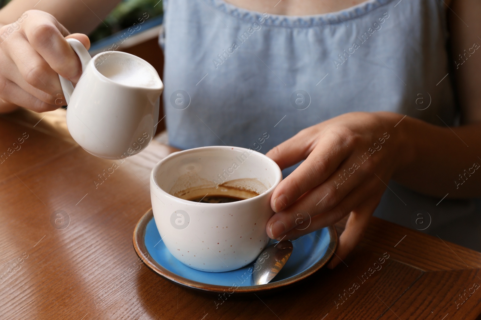 Photo of Woman adding milk to fresh aromatic coffee at table, closeup