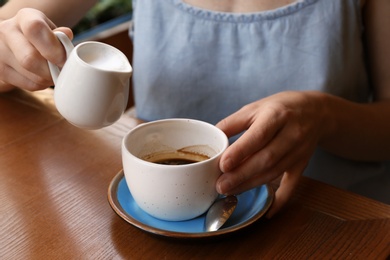 Woman adding milk to fresh aromatic coffee at table, closeup