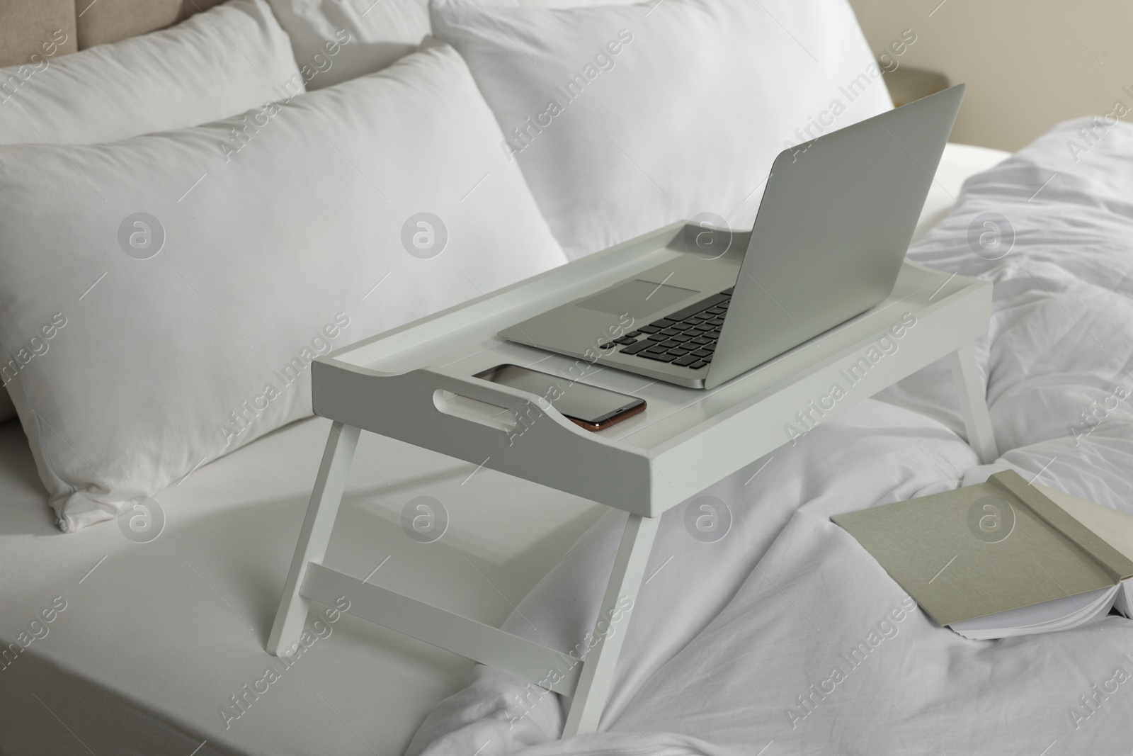 Photo of White tray with modern laptop and smartphone on bed indoors