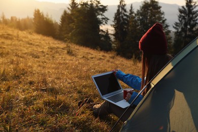 Photo of Woman working on laptop near camping tent outdoors surrounded by beautiful nature