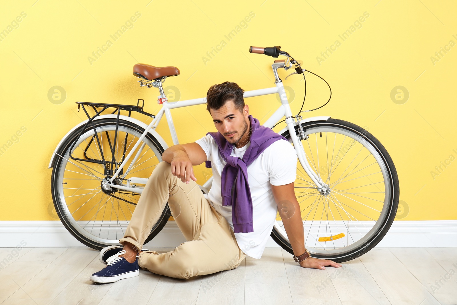 Photo of Handsome young hipster man sitting with bicycle near yellow wall