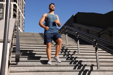 Photo of Happy man running down stairs outdoors on sunny day, low angle view