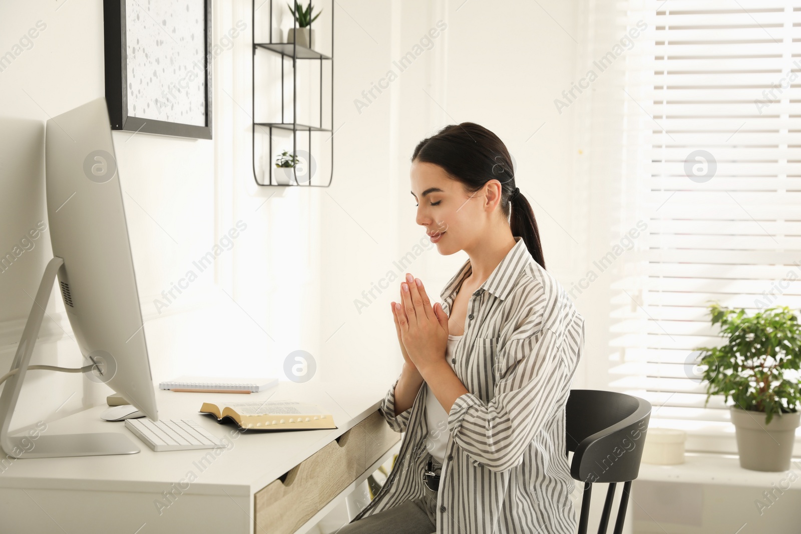 Photo of Beautiful young woman praying over Bible at desk