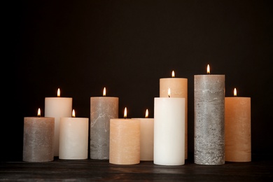 Photo of Alight wax candles on table against dark background