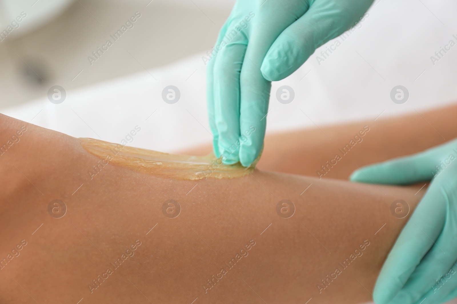 Photo of Woman getting wax epilation of legs in salon, closeup