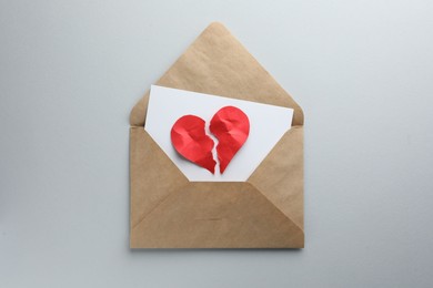 Photo of Envelope with halves of torn red paper heart on white background, top view. Broken heart