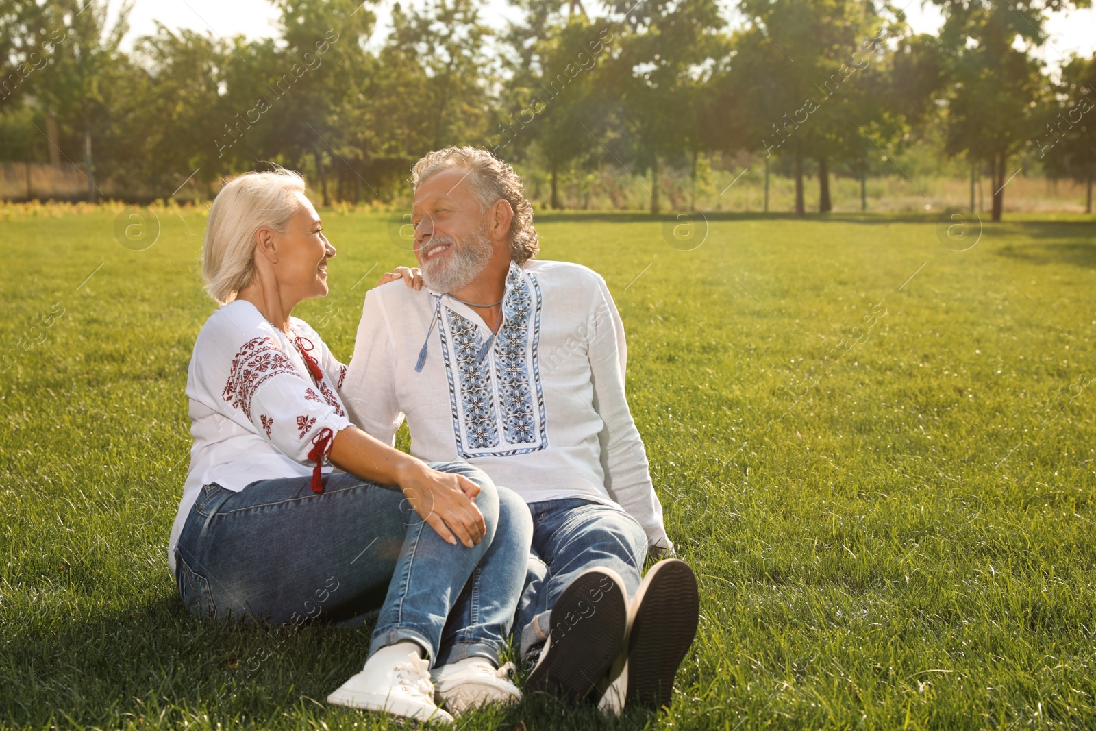 Photo of Happy mature couple in Ukrainian national clothes resting on green grass outdoors