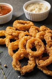 Photo of Homemade crunchy fried onion rings and sauces and sauces on slate plate, closeup