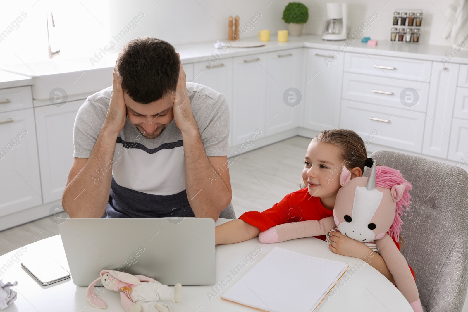 Photo of Cute child disturbing stressed man in kitchen. Working from home during quarantine