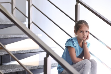 Depressed preteen girl sitting alone on stairs. Space for text