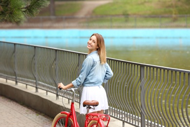 Beautiful woman in casual outfit with bicycle on bridge over pond