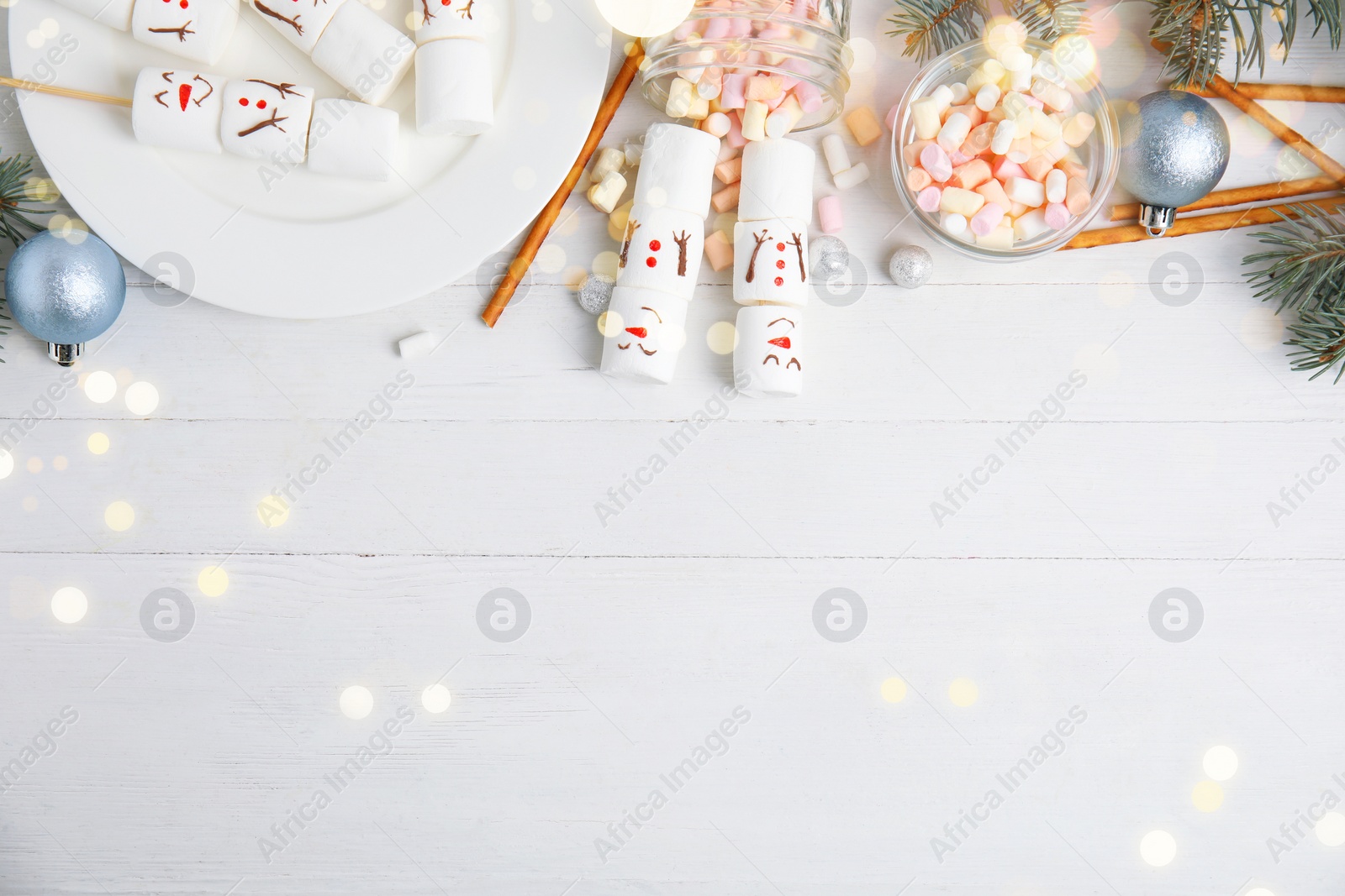 Image of Flat lay composition with funny snowmen made of marshmallows on white wooden table, space for text. Bokeh effect 