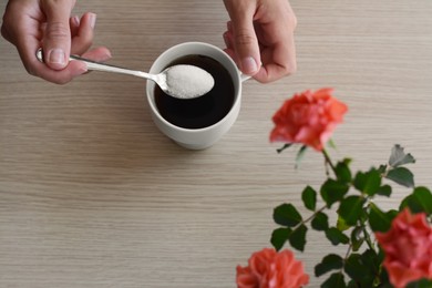 Photo of Woman adding sugar to morning coffee at wooden table, top view