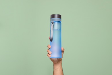 Photo of Man holding transparent plastic bottle of water on light green background, closeup