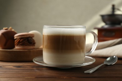 Photo of Aromatic coffee in cup, macarons and spoon on wooden table, closeup