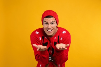 Emotional man in Christmas sweater and hat on yellow background